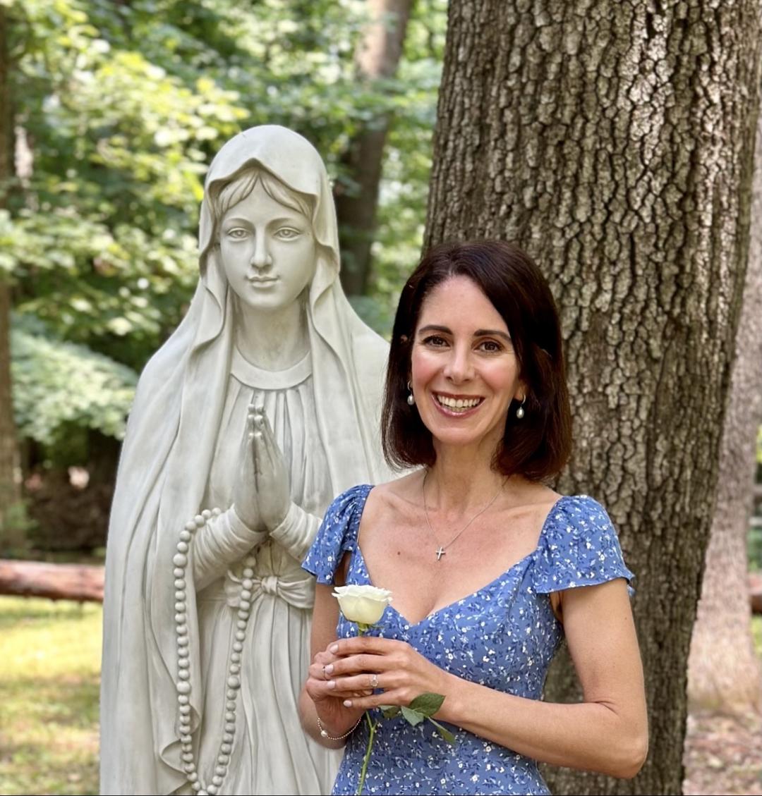 Michelle Christine holding a white rose beside a statue of Our Lady